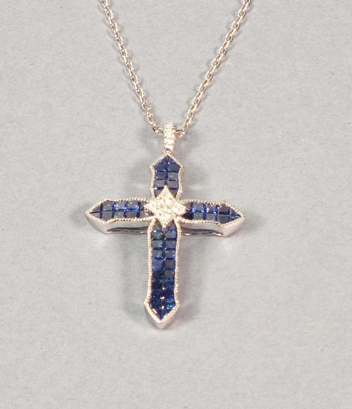 A 18ct white gold sapphire and diamond cross, pave set sapphires within a diamond border and diamond