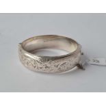 A hollow hinged silver bangle with scroll decoration 27g