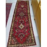 A hand knotted woollen runner with a red field, 293cm x 97cm