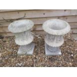 A pair of stone effect urns on stands, 52cm tall x 35cm