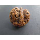 A well carved Oriental walnut shell, 4.5cm wide, depicting sages and tiger, with good colour and