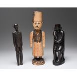 Three East African figures including a seated hunchback male figure with large pierced ears and
