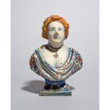 A small Delft bust of a woman, 18th century, wearing a low cut floral patterned robe, a cross
