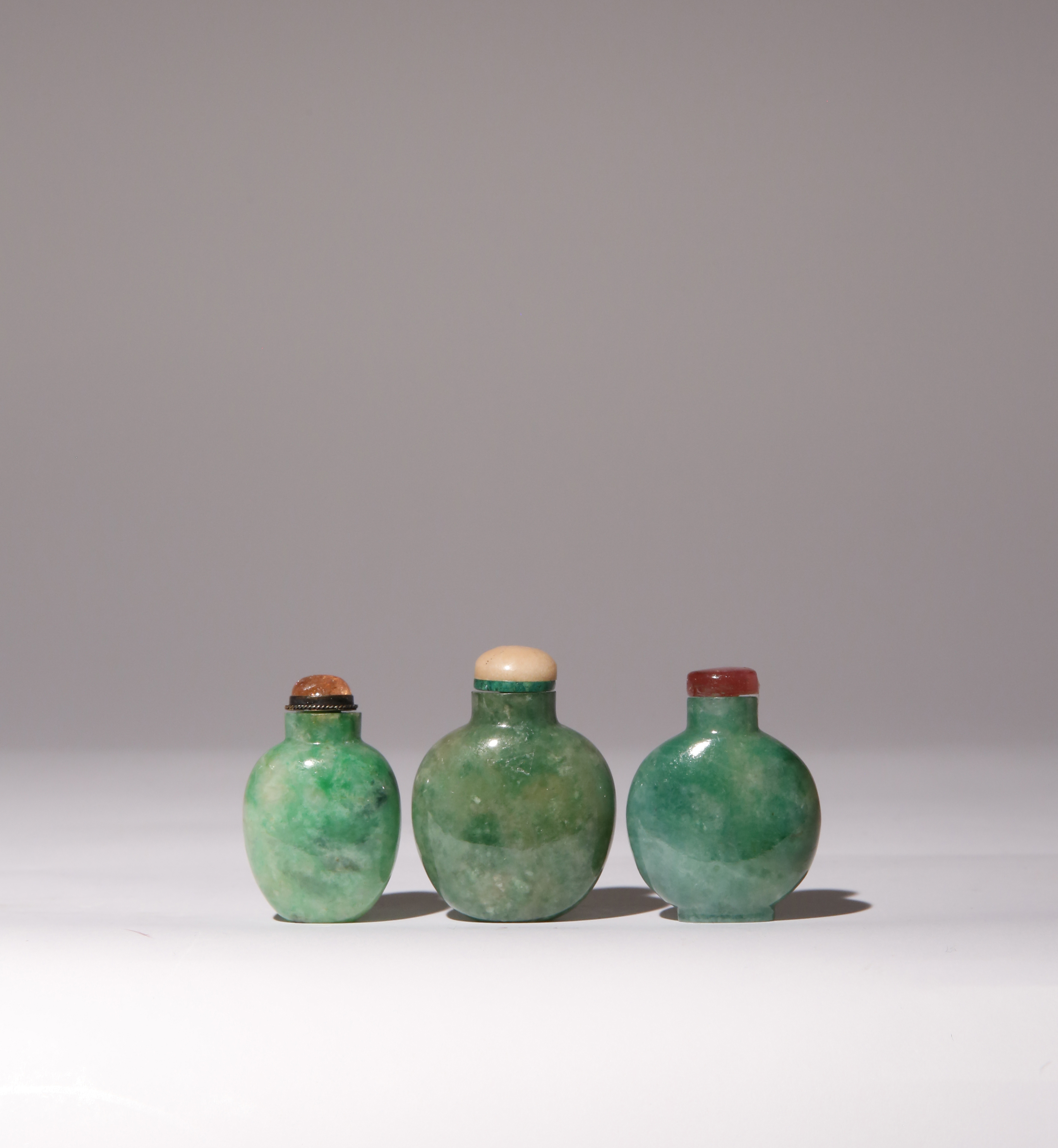 THREE CHINESE JADEITE SNUFF BOTTLES QING DYNASTY Each of flattened ovoid shape, the apple-green