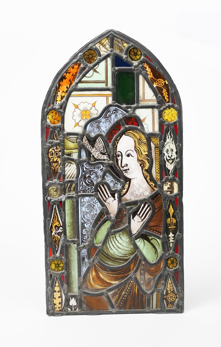A stained glass panel of The Annunciation, arched rectangular panel, inside border of grotesque