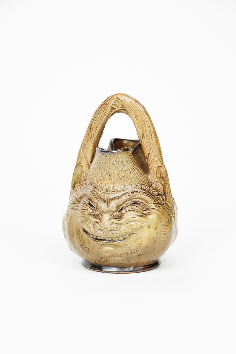 An unusual Martin Brothers stoneware grotesque face jug, dated 1890, modelled in low relief with a