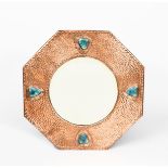 An octagonal copper mirror, hammered finish, applied with four Ruskin blue ceramic hearts set in