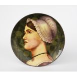 A Doulton Lambeth Faience charger, painted with a maiden in profile, before fruiting boughs, in