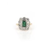 An emerald and diamond ring, of cluster design. millegrain-set with a step-cut emerald weighing