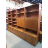 A run of G plan teak sectional lounge wall units enclosed by an arrangement of cupboards and