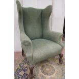 A late 19th century upholstered wing chair, in an 18th century manner with scrolled arms, raised