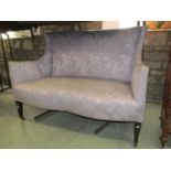 An Edwardian two seat sofa with shaped outline, shallow winged back, serpentine shaped seat and