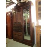 An Edwardian mahogany compactum wardrobe enclosed by three doors and four long drawers, mirror and