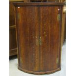 A Georgian oak bowfronted hanging corner cupboard enclosed by a pair of doors with brass fittings