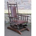 An Edwardian child's size rocking chair with leather upholstered pad seat and back within a turned