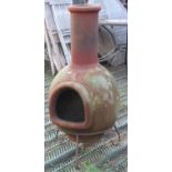 A weathered terracotta chimenea raised on a simple iron stand, 102cm high