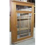 A stripped and waxed pine hanging corner cupboard enclosed by a glazed panelled door, fitted with