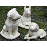 Three composition stone garden ornaments in the form of dogs in varying pose, all with cream painted