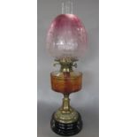 A Duplex oil lamp with a brass stand and an orange faceted font and a fading cranberry shade, 57