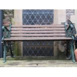 A garden bench with hardwood lathes and green painted cast iron end supports with decorative bound