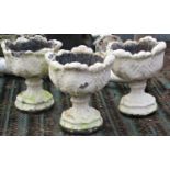 Three cast composition stone garden urns with circular acanthus leaf bowls raised on foliate