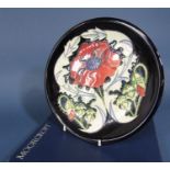 A Moorcroft plate with art nouveau style poppy decoration on a dark blue ground with impress and