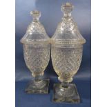 A pair of cut glass urns with diamond cut design, with covers, raised on a square base.