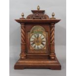 A 19th century bracket clock in an oak case with spiral column supports and broken arch brass dial