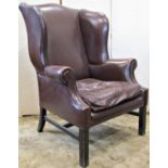 A vintage Georgian style dark brown leather upholstered wing armchair with shaped outline and