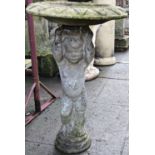 A weathered two sectional cast composition stone bird bath with standing cherub pedestal