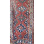 An antique middle eastern corridor rug with interlocking medallions upon a red ground, 210cm x 113cm