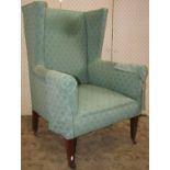 An Edwardian wing armchair with green ground repeating floral sprig patterned upholstery raised on
