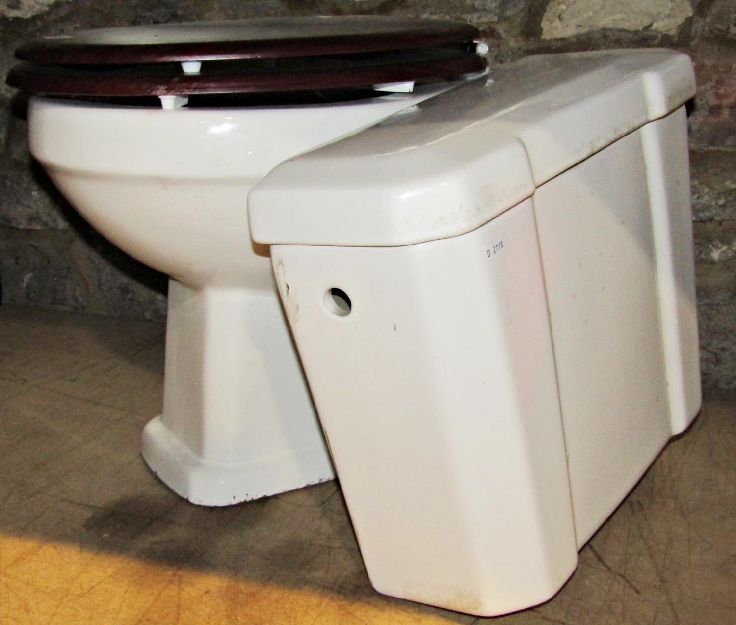 A white glazed ceramic toilet with chrome pipe and flush box cistern and fittings