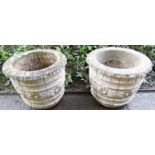 A pair of weathered cast composition stone circular planters with repeating flower head banded and