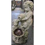 A weathered cast composition stone garden water feature in the form of two cherubs, one supporting