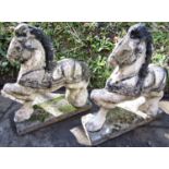 A pair of weathered composition stone garden ornaments in the form of standing horses with partially
