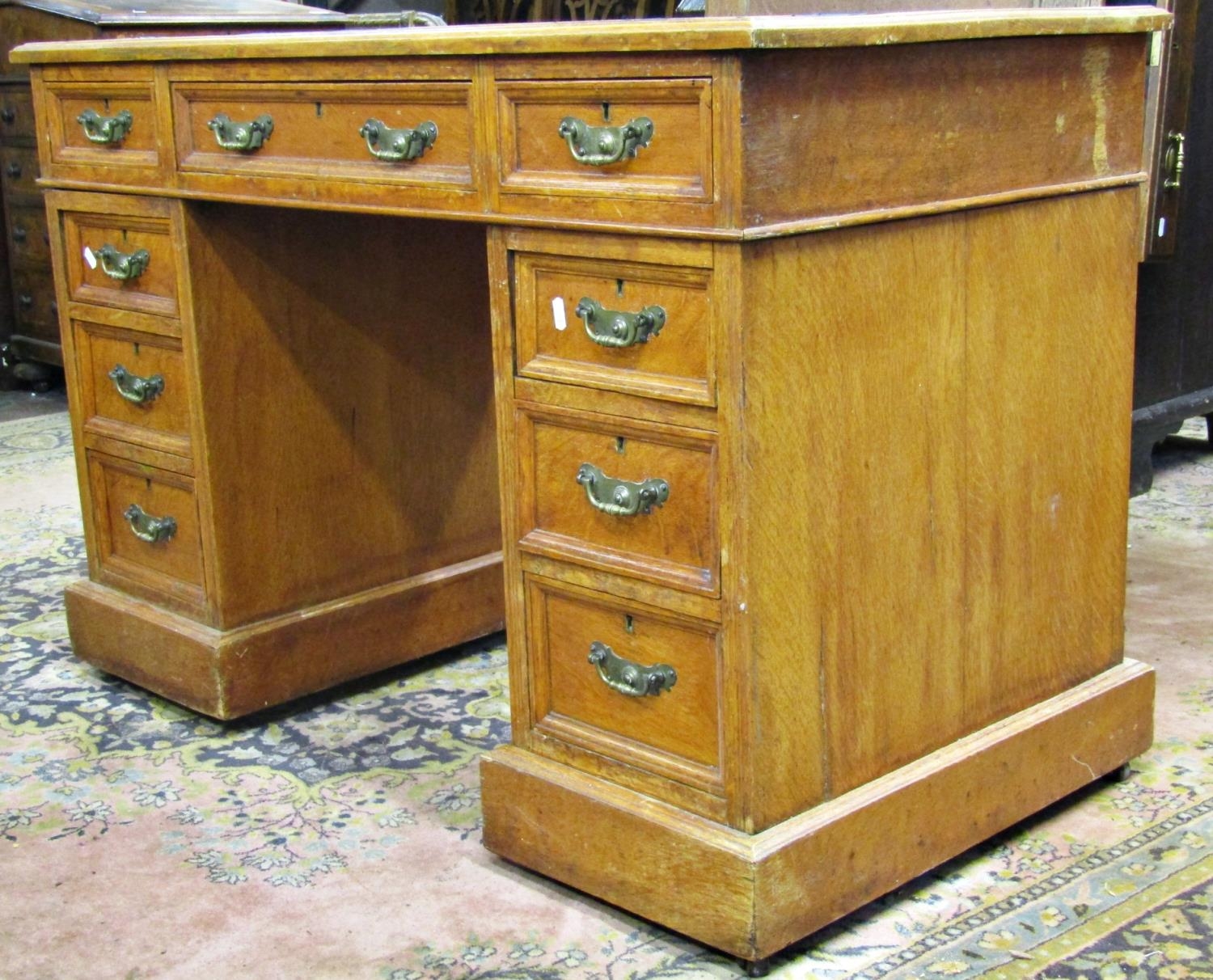 An late Victorian oak pedestal desk of nine graduated drawers with brass plate handles and inset