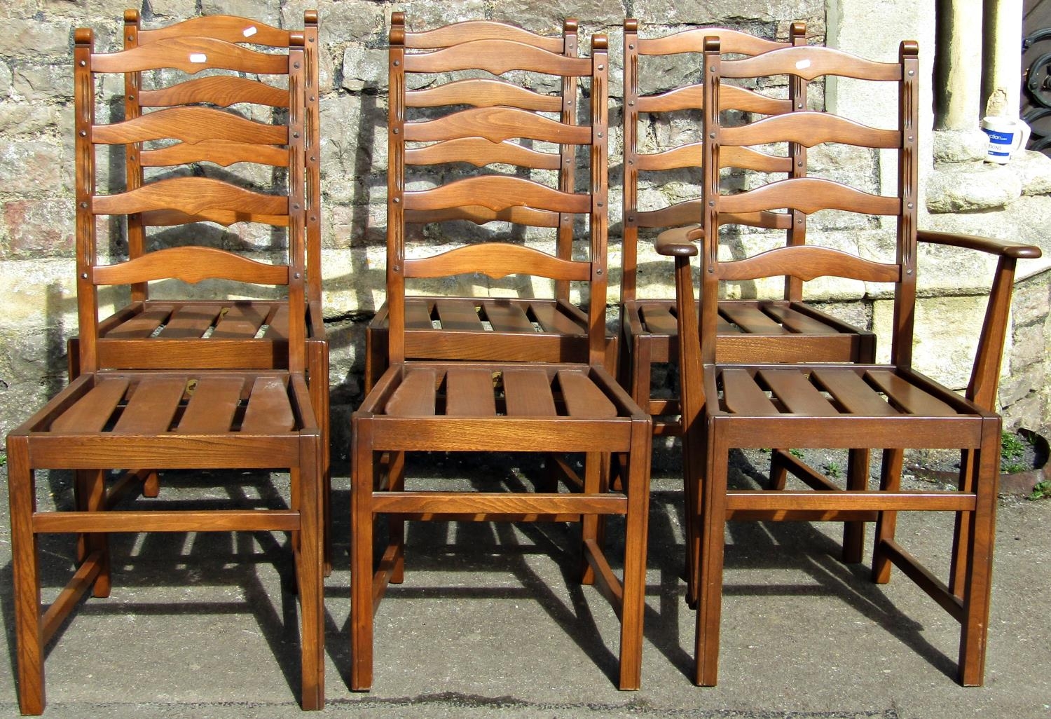 A set of six (5&1) Ercol stained elm wavy ladderback dining chairs with slatted seats, raised on