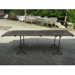 A pair of old iron work trestles with simple swept supports with associated pine boarded top, the