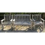 A weathered teak three piece garden suite comprising two seat bench and a pair of matching armchairs