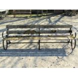 A vintage park or garden bench with weathered timber slatted seat and low back rails, raised on