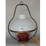 A hanging oil lamp with an opaque white glass shade and a red glass font, converted to an electric