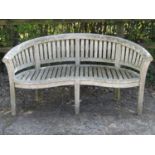 A weathered teak banana shaped garden bench with slatted seat and back, 164cm long