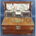 A Victorian oak games tantalus with brass overlay, having three matching decanters and two