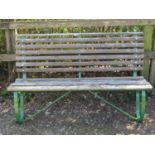 A vintage garden bench with weathered timber lathes, raised on green painted heavy gauge sprung