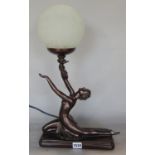 A bronze effect Art Deco style table lamp of a dancing girl holding aloft a globular shade.