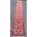 A Malayer runner with overall floral pattern on a red ground, 400 x 83cm