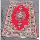 A Kashan rug with central floral pattern medallion on a red ground within foliate running borders,