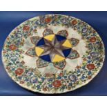 A large glazed ceramic wall hung platter with an inner geometric design and floral border. 63cm