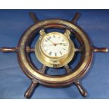 An old ships wheel in teak with brass mounts, supporting a later applied brass bulkhead clock set